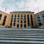 Exterior do prédio do Federal Reserve, visto de baixo, com bandeiras dos Estados Unidos e escadaria.