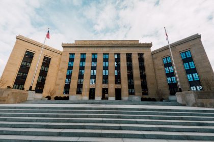 Exterior do prédio do Federal Reserve, visto de baixo, com bandeiras dos Estados Unidos e escadaria.