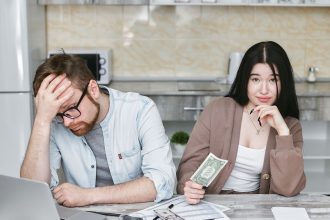 Casal analisa as finanças e organiza o orçamento sobre a bancada de uma cozinha.