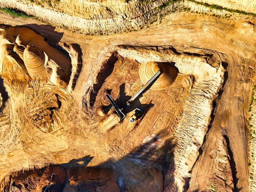 Vista aérea de uma extensa mina a céu aberto, com máquinas pesadas escavando o terreno.