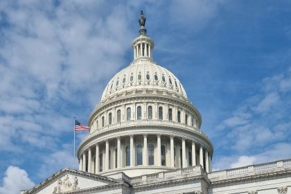 Cúpula do Capitólio dos Estados Unidos, com a bandeira americana sob um céu azul.