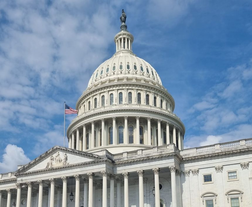 Cúpula do Capitólio dos Estados Unidos, com a bandeira americana sob um céu azul.