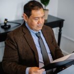 Advogado, visto de cima, analisa atentamente um relatório em uma pasta sobre uma mesa de escritório.