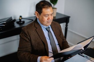 Advogado, visto de cima, analisa atentamente um relatório em uma pasta sobre uma mesa de escritório.