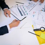 Documentos com gráficos e relatórios financeiros espalhados sobre uma mesa de trabalho.