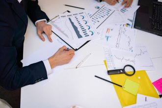 Documentos com gráficos e relatórios financeiros espalhados sobre uma mesa de trabalho.