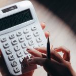 Mãos usando uma calculadora e uma caneta para fazer cálculos financeiros.