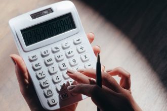 Mãos usando uma calculadora e uma caneta para fazer cálculos financeiros.