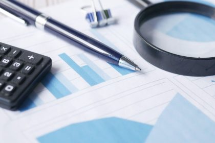 Calculadora, caneta e lupa sobre documentos financeiros, simbolizando a análise detalhada de riscos de crédito.