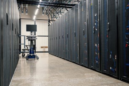 Fileiras de gabinetes metálicos com servidores, dispositivos de rede e cabos em um data center moderno.