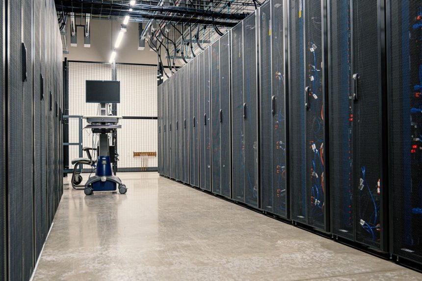 Fileiras de gabinetes metálicos com servidores, dispositivos de rede e cabos em um data center moderno.