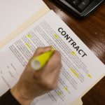 Pessoa destacando trechos de um contrato financeiro sobre uma mesa de escritório.