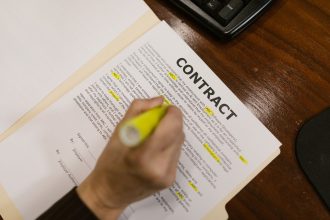 Pessoa destacando trechos de um contrato financeiro sobre uma mesa de escritório.