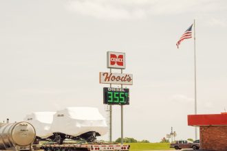Posto de combustível rural nos Estados Unidos com bomba de diesel, caminhões estacionados e bandeira americana.