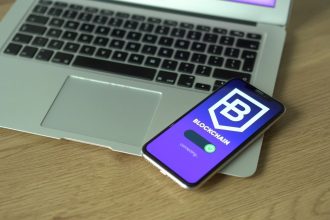 Smartphone exibindo uma aplicação de blockchain apoiado sobre um laptop, em representação de tecnologia financeira digital.